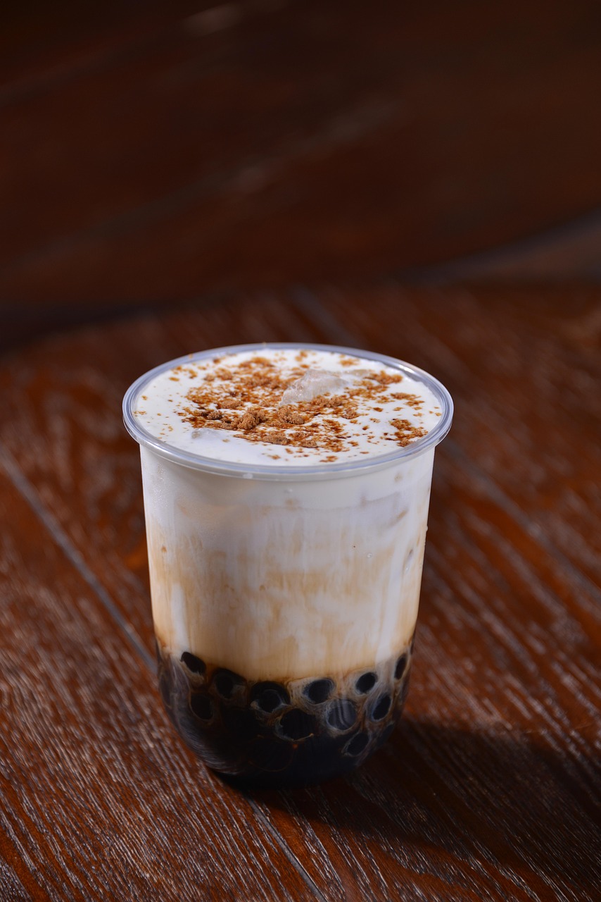 A layered brown sugar milk tea with boba pearls and syrup at the bottom sits in a cup, topped with foam and a sprinkle of cinnamon.