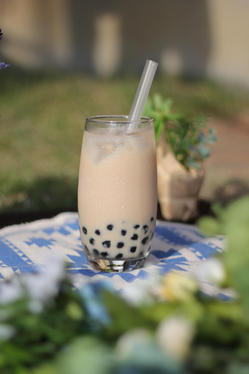 A classic milk tea with boba pearls sits outdoors on a blue and white cloth, with grass visible in the background.