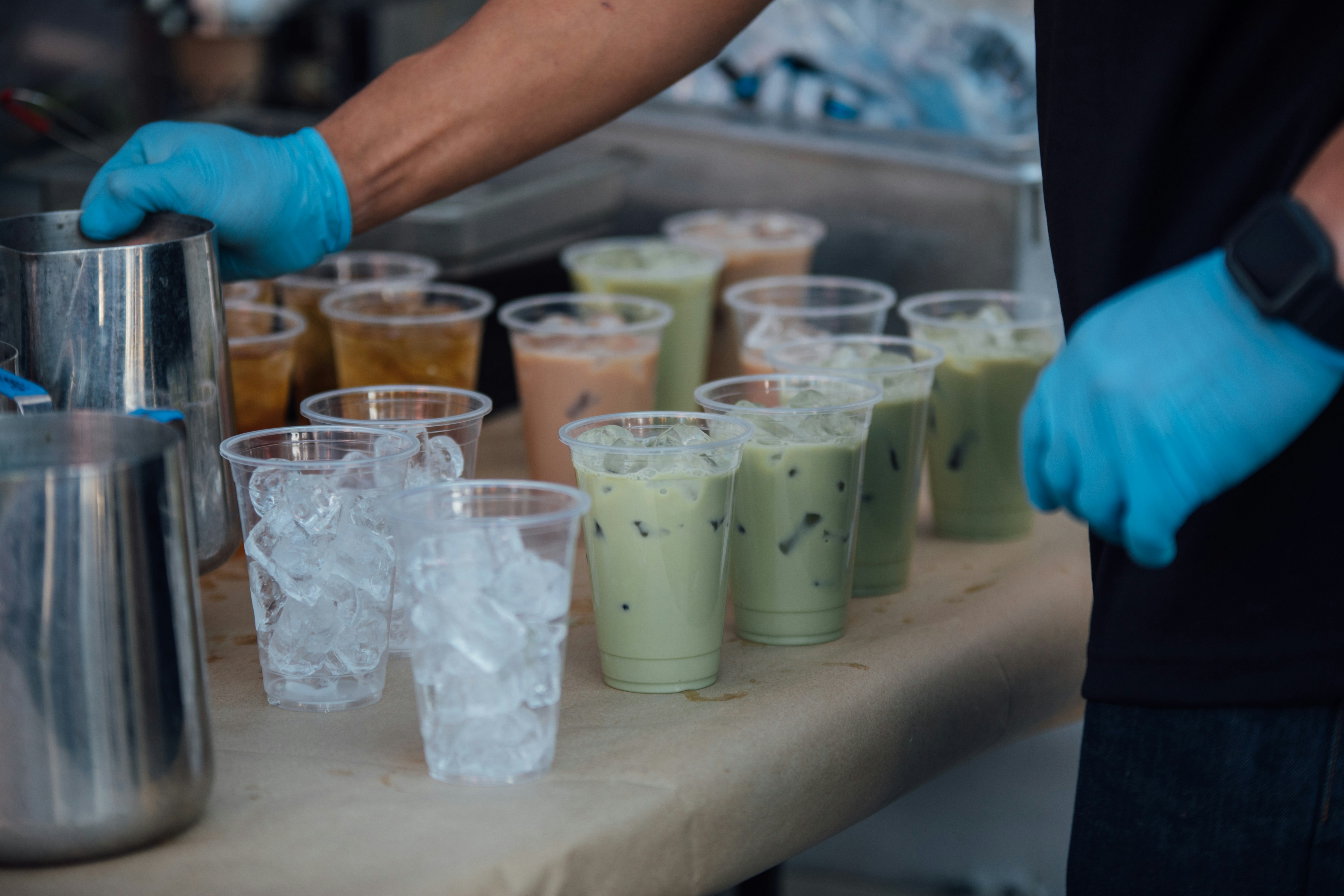 An employee pours matcha into a cup at a table filled with prepped drinks, including matcha lattes and Thai tea, ready to be served.